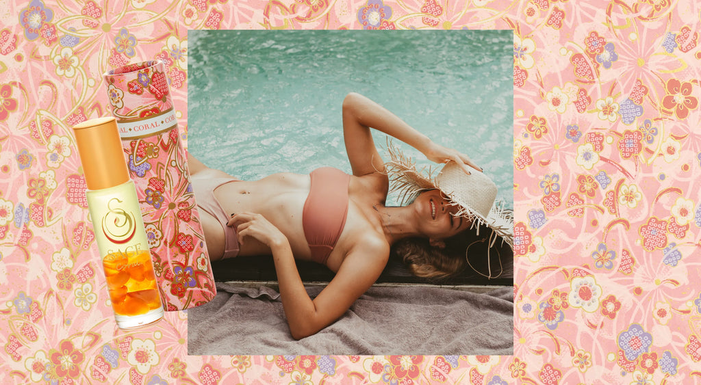 Image of coral glass bottle with crystal infront of girl with straw hat laying on a towel next to water