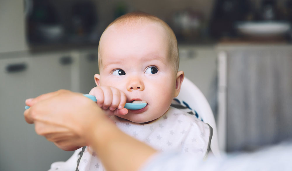 Baby boy grabbing s spoon from mum