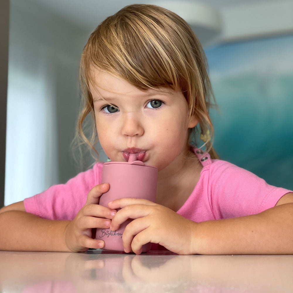 toddler girl drinking smoothie from silicone cup with lid and straw