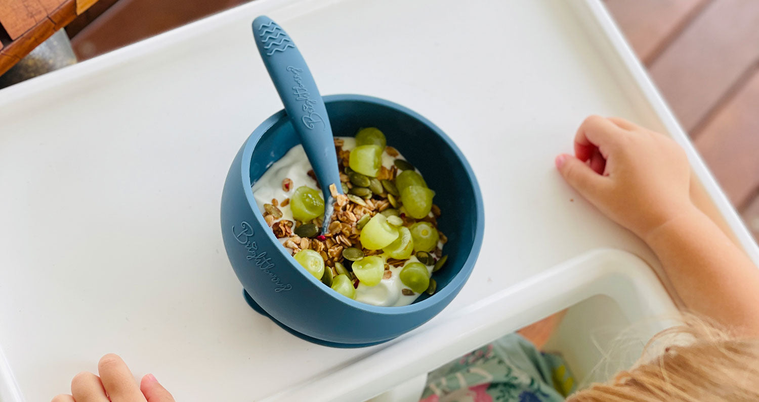 Brightberry bowls bebé comiendo uvas, yogur y cereales sentado en una silla alta