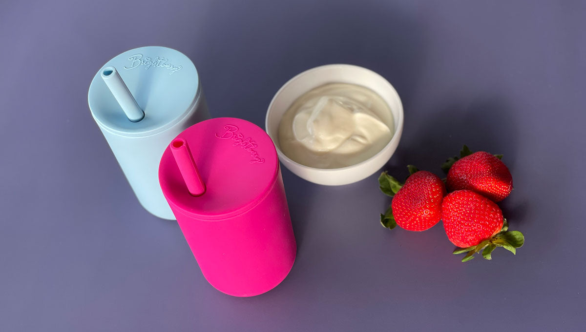 kids silicone smoothie cups in blue and pink colours wit yogurt and strawberries