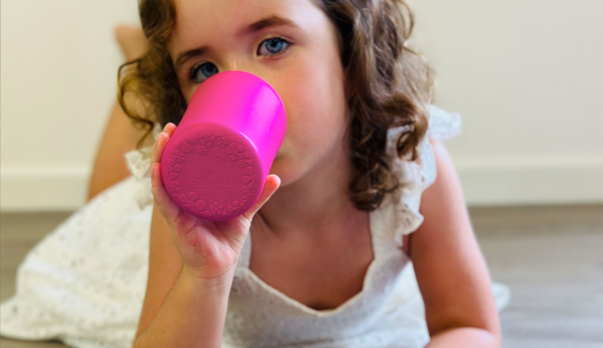 Niña pequeña bebiendo de una taza de batido rosa brillante para niños