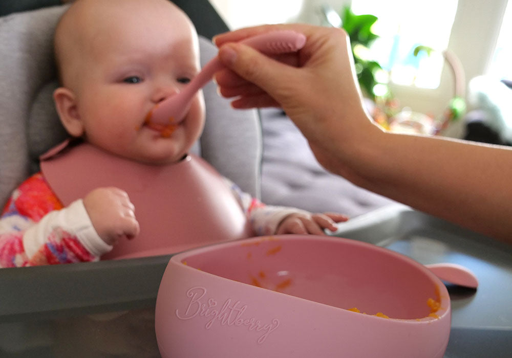 El bebé comienza a tomar sólidos al ser alimentado con cuchara con comida que mamá prepara en un recipiente de succión de silicona y una cuchara de silicona.