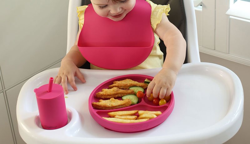 Bebé feliz explorando comida en un plato de silicona dividido