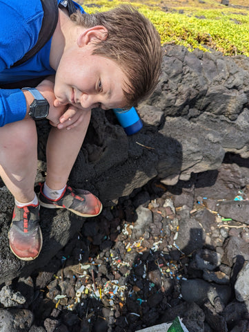 Young child sitting near plastic waste on a beach
