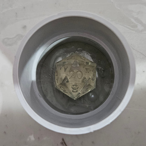 A d20 placed inside a PVC pipe coupling used as a mold housing.