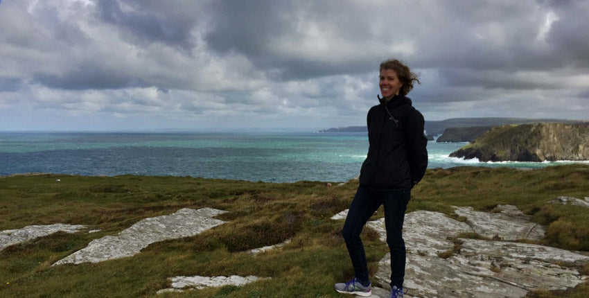 Holly Press Fibers' owner, Elizabeth, glancing at the camera on a wonderfully windy day at Tintagel with the sea in the background.