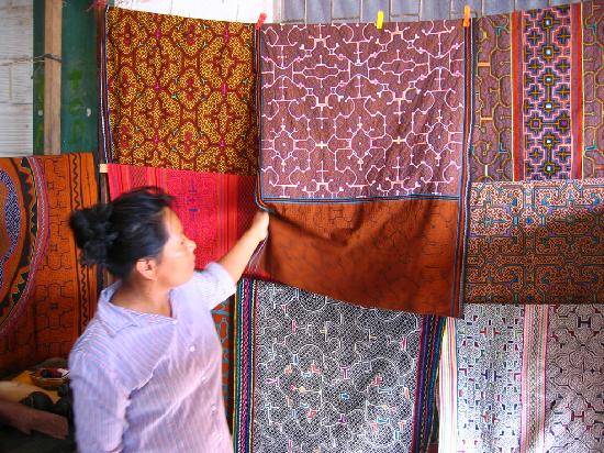 a woman stands in front of several quilts with intricate patterns