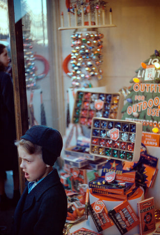 A vintage photograph of a young boy standing in front of a Christmas themed store display