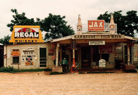 A vintage color photo feauturing a crossroads store advertising various types of alcohol