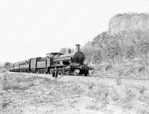 A vintage photograph of a man standing next to a train as it passes in front of mountains