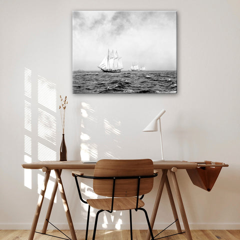 A digital mockup of a canvas print of a vintage photograph of three ships at sea, hanging above a desk