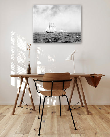 A canvas print reproduction of a photo of three ships hanging on a wall above a desk