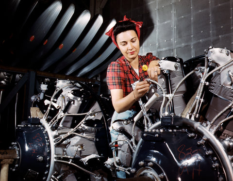 A vintage photograph of a woman working on an airplane motor