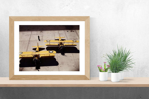 A small framed paper print of a vintage color photograph of Navy Planes sitting on a ledge