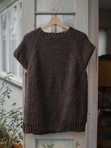 progress photo of a grey handspun and hand knit sweater. It hangs on an external French door from a coat hanger and still needs the sleeves knit