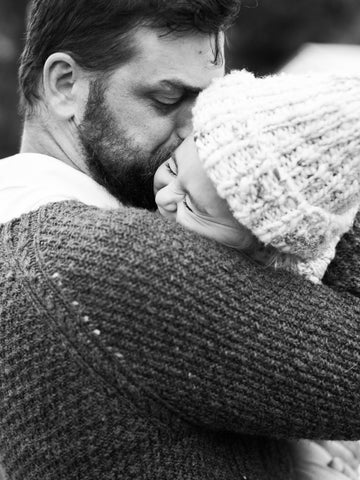 black and white photo of a man kissing his daughter on the cheek. both wear handspun and knit garments