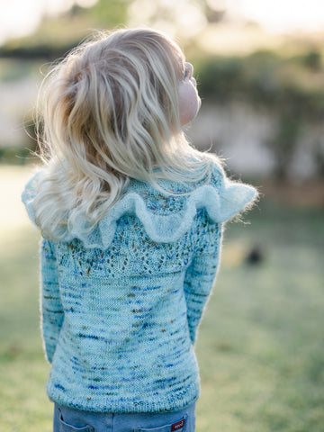 young blonde girl looking up to the right shot from behind to show lace and ruffle detail on back of sweater