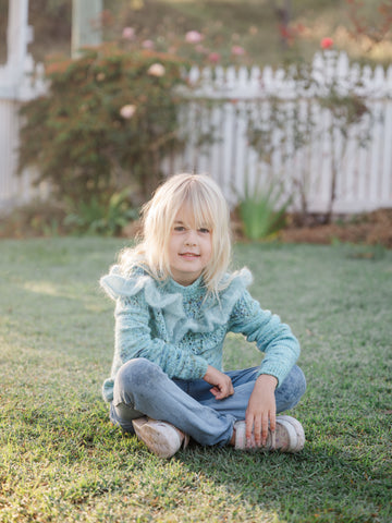 young blonde girl sitting and looking into the camera to show off hand knit sweater