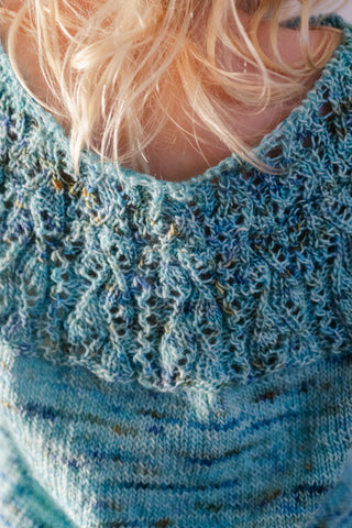 back view of an unfinished sweater which is held on circular knitting needles during a fit check on a young girl