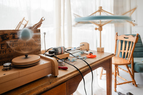 yarn is wound from a ball winder from a wooden umbrella swift. The table is covered with various crafting paraphernalia