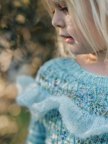 close up of ruffle and hand knit effervescent mini sweater as young blonde girl looks to left