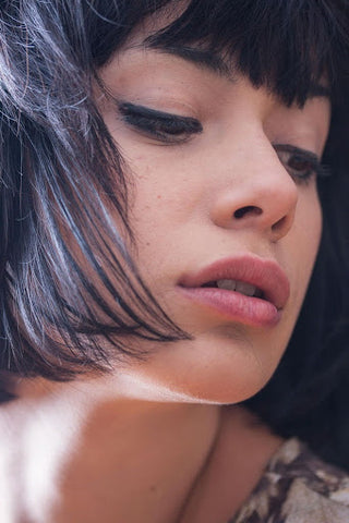 A young woman with purple, short hair glancing over her shoulder. Source: Pexels.