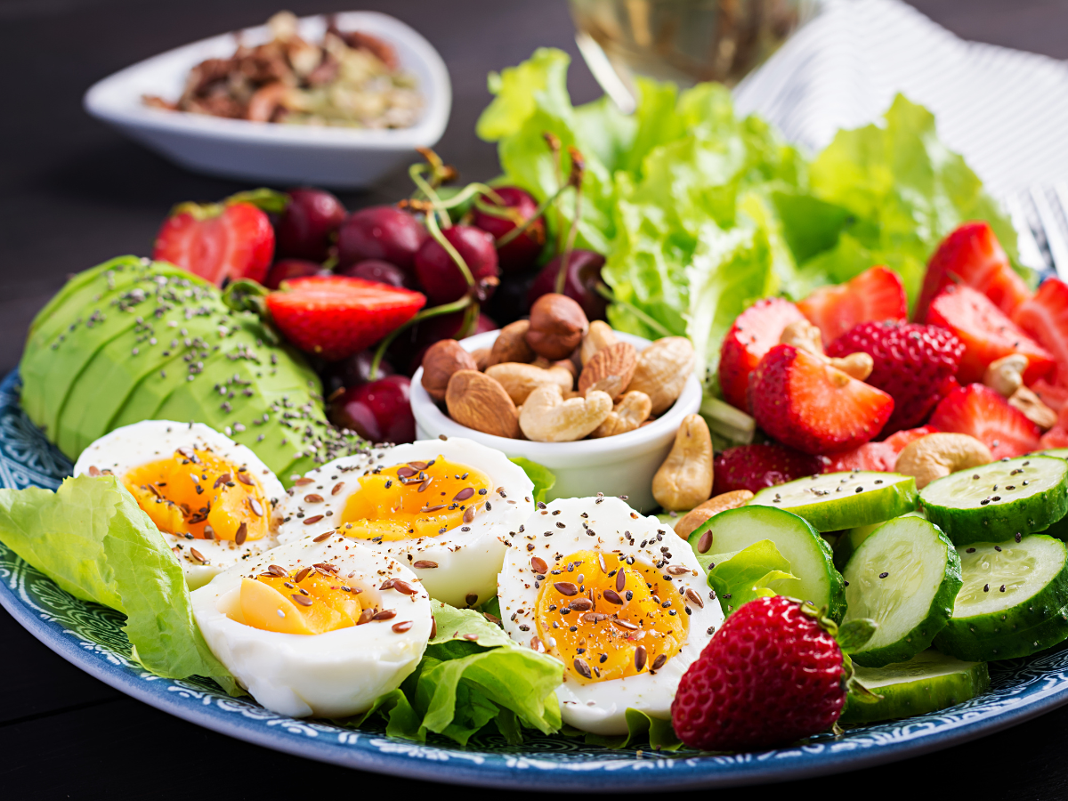 A plate full of paleo friendly, caveman diet snacks such as eggs,avocado, mixed greens a variety of nuts and fresh fruit.