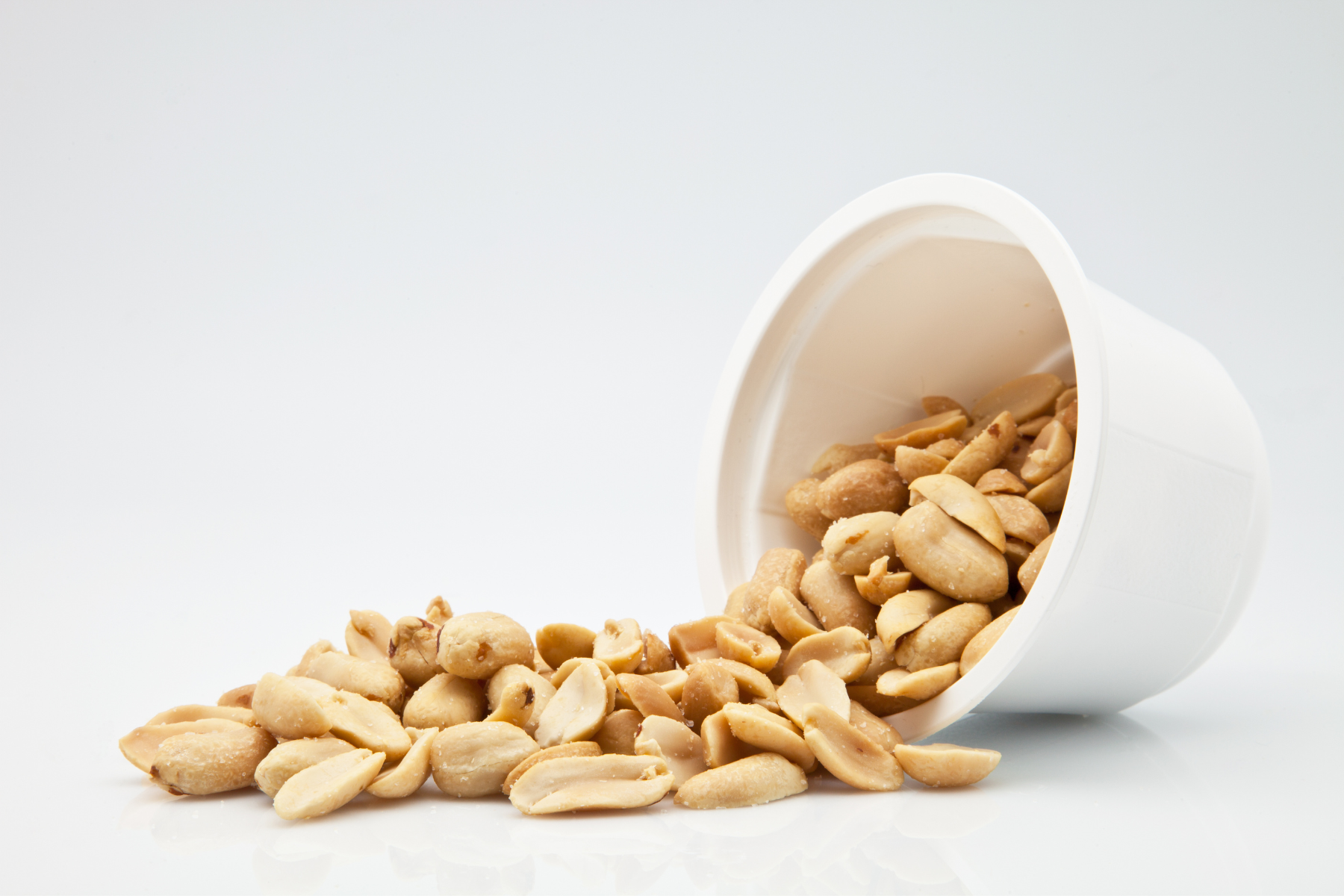 A bowl of roasted peanuts, tipped over onto a white counter.