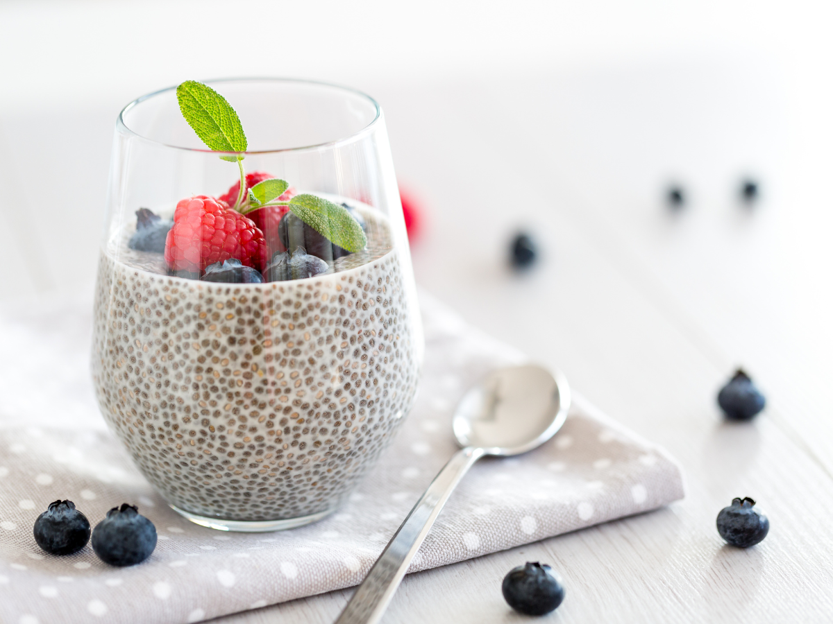 A glass of chia seed pudding, prepared with coconut milk and topped with fresh strawberries and blueberries making for a great Paleo-friendly breakfast as part of a Paleo Diet Meal Plan