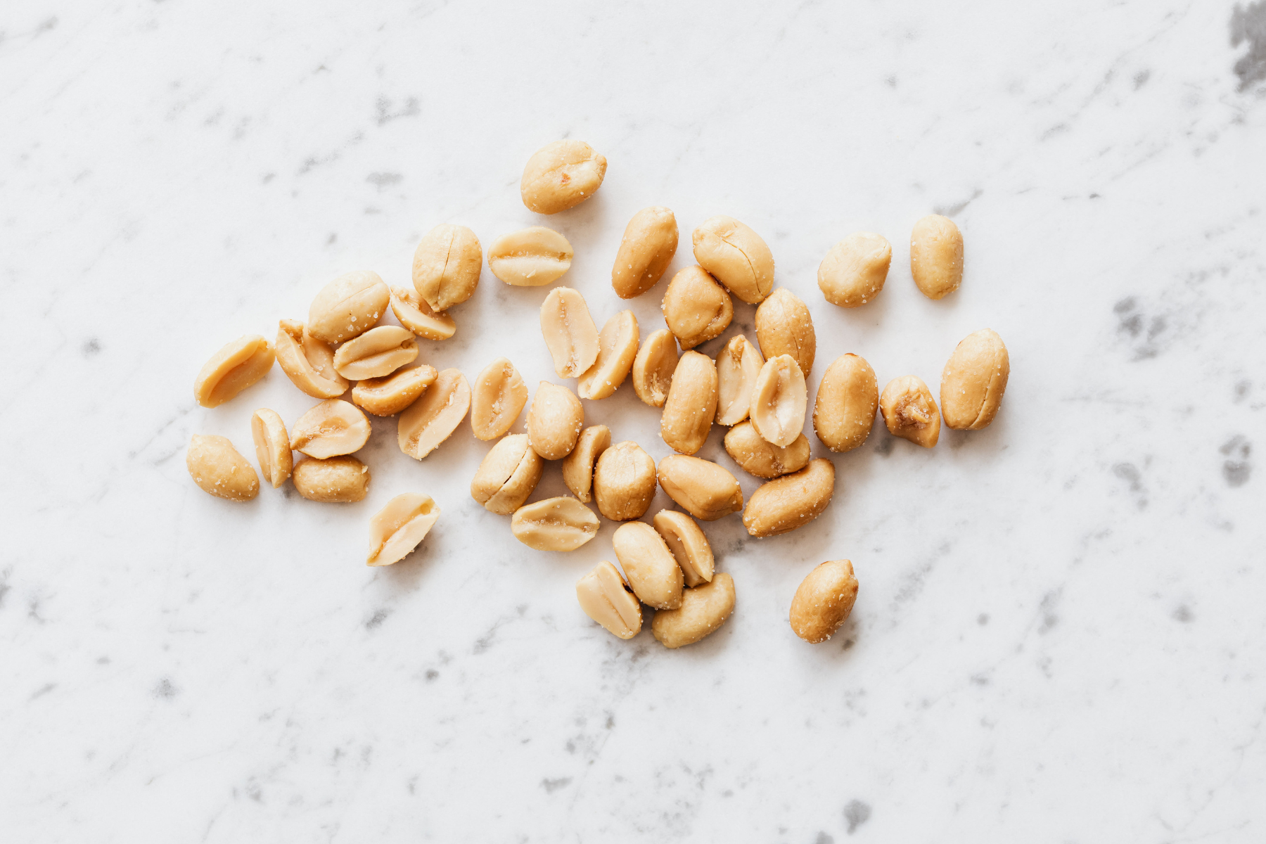 A handful of roasted peanuts scattered on a white marble table