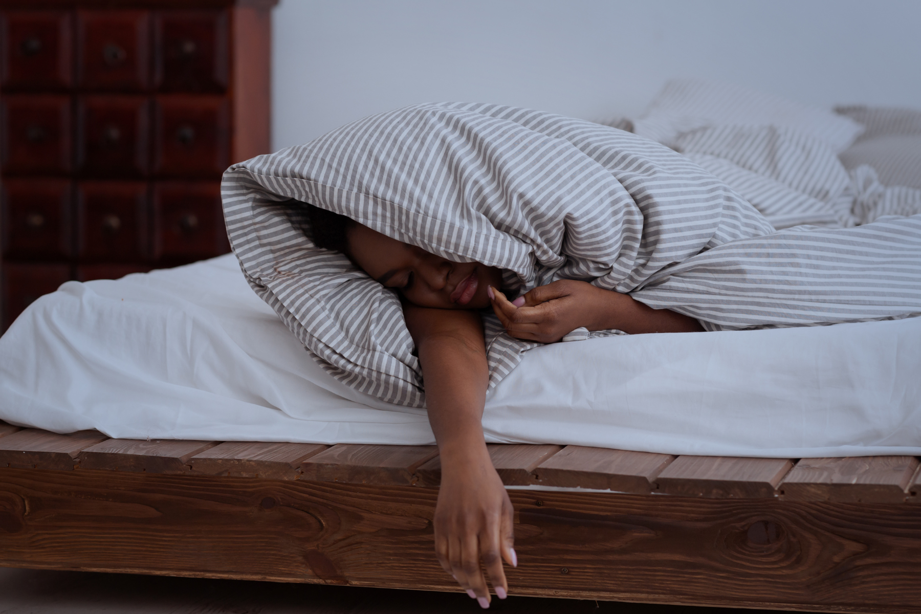 Image of a woman sleeping on a bed, arm under a blanket, depicting the challenges of menopause-related sleep disturbances.