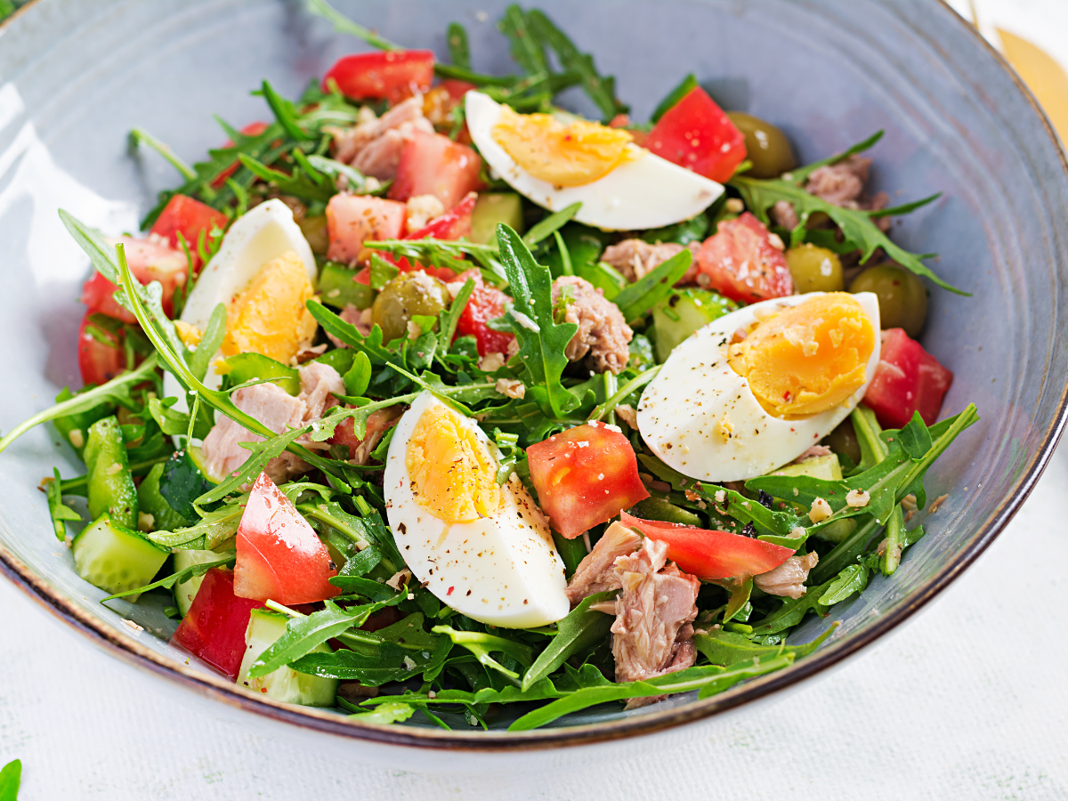A bowl of tuna salad containing eggs, tomatoes, mixed leaves and cucumber as part of a paleo diet meal plan.