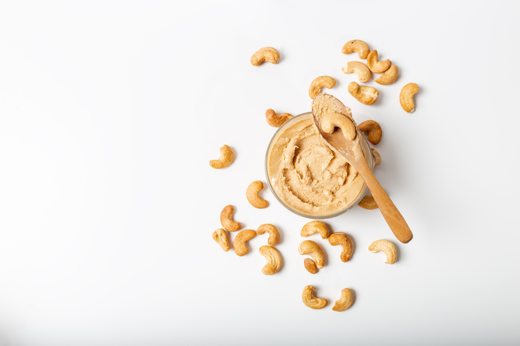 cashew butter in a bowl against a white background with some loose cashews scattered around it.
