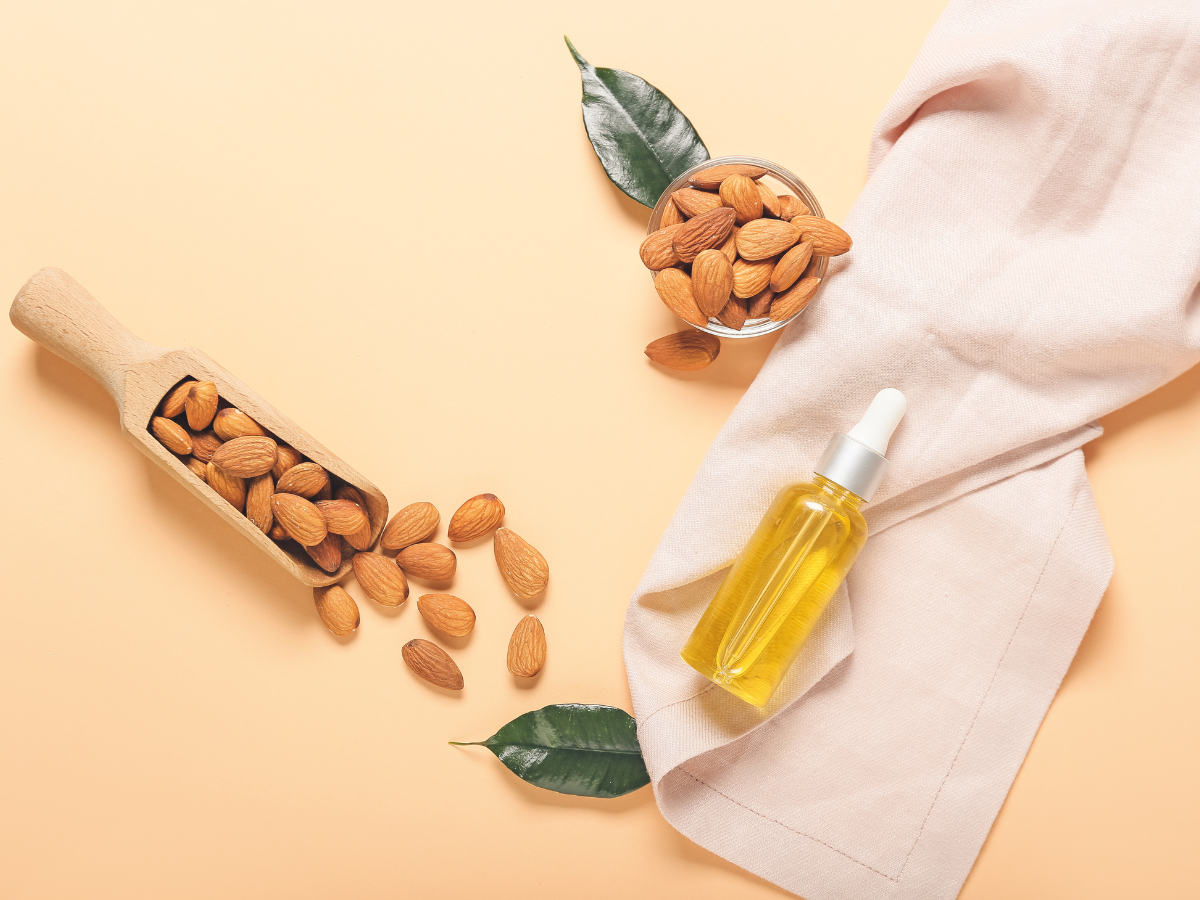 Almonds and almond oil against a pink background.