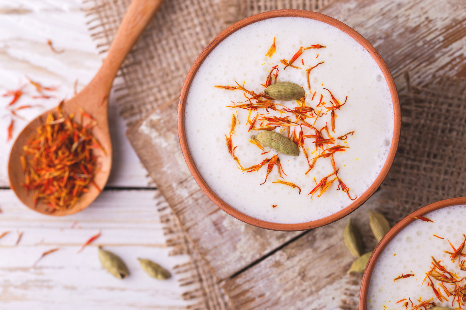 a mug of saffron milk garnished with cardamom pods sitting next to a spoon of saffron.