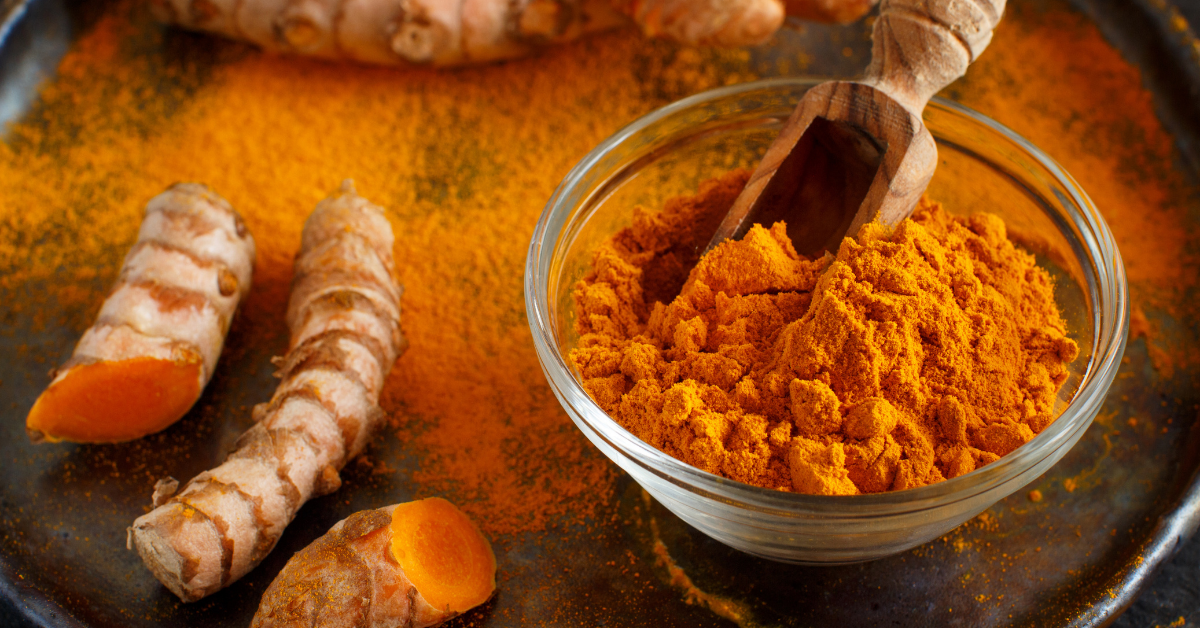 curcumin in a bowl with a wooden shovel in it next to fresh curcumin