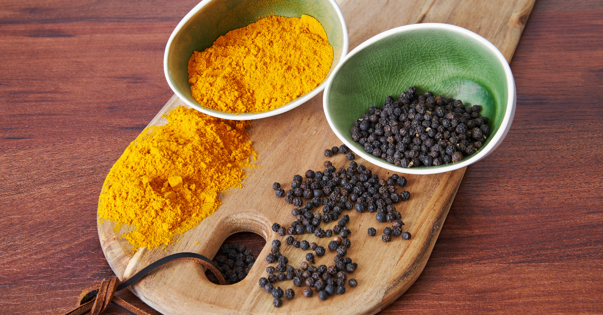 small bowl of dried tumeric and bowl of black pepper on a wooden board