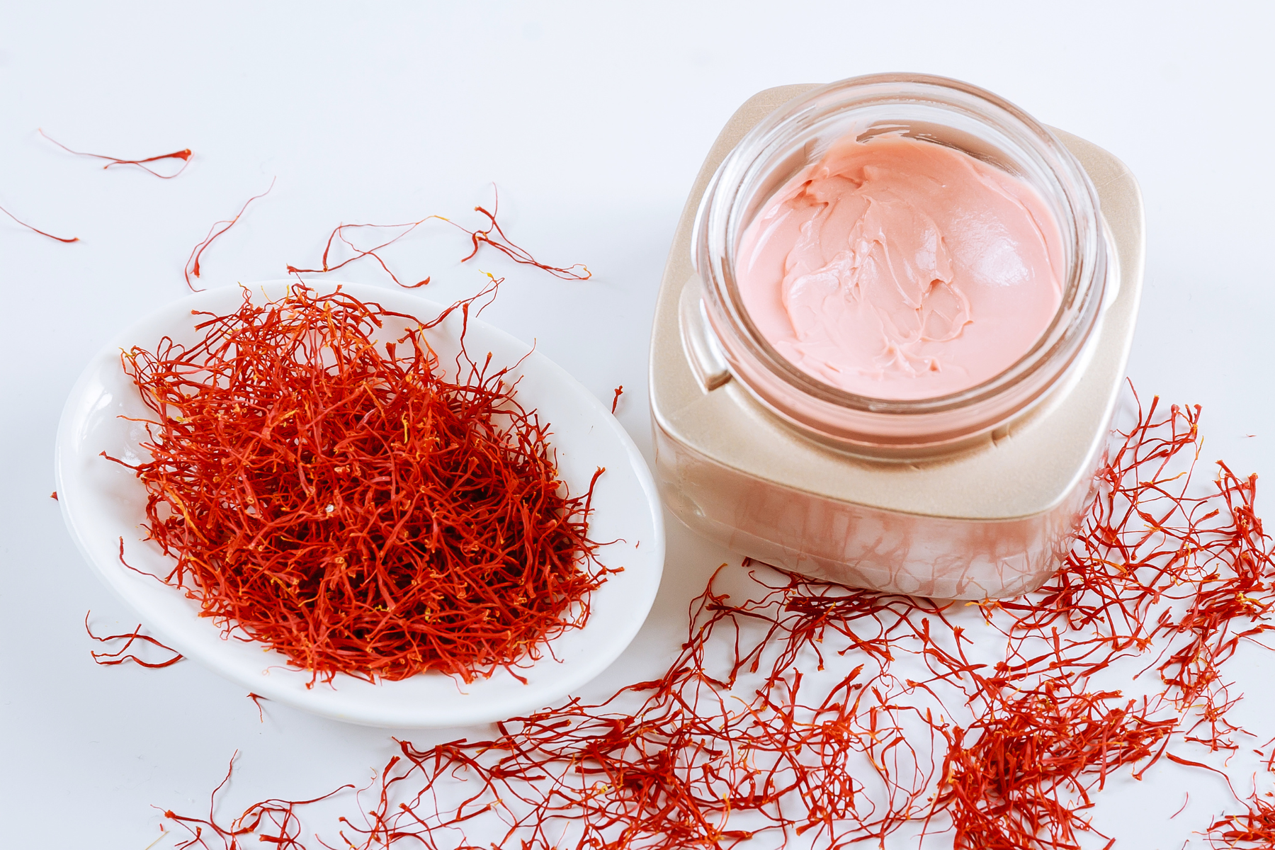 A jar of saffron face cream and a bowl of dried saffron, a vibrant and aromatic spice used in cooking and medicine.