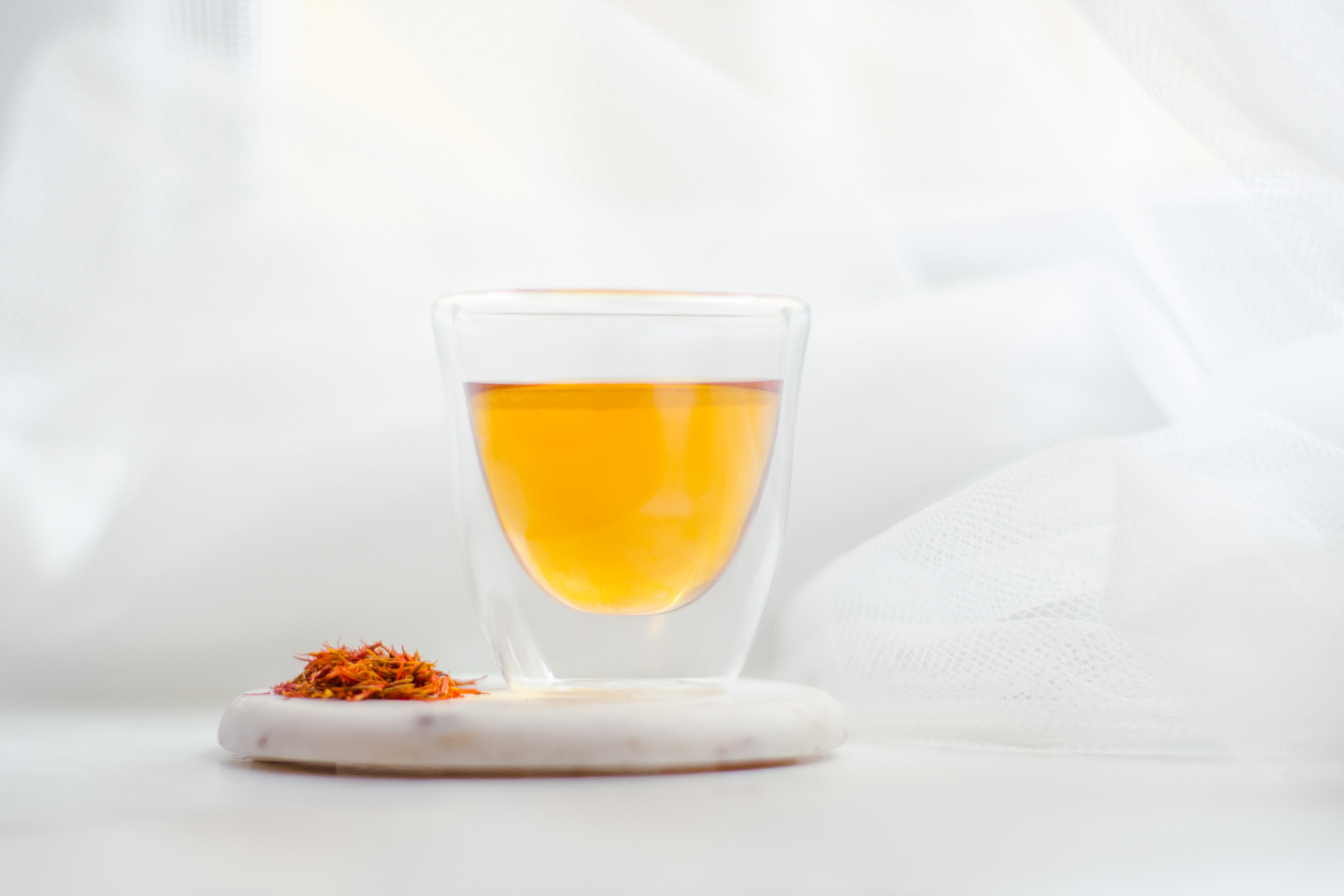 A glass of orange juice on marble, accompanied by saffron tea on a white table and loose saffron.