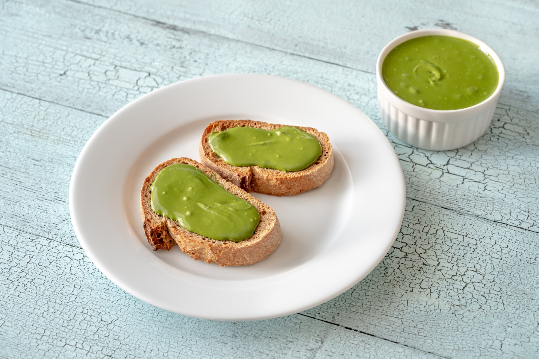 A plate of toast spread with pistachio nut butter, next to a bowl full of pistachio nut butter.