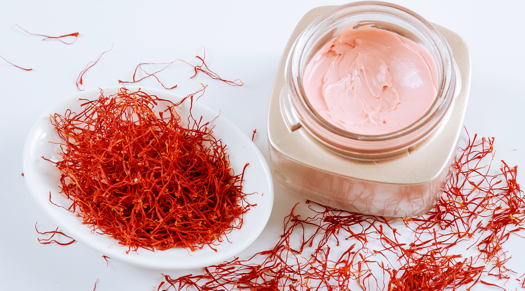 A skincare-focused image featuring a jar of saffron infused face cream and a bowl of dried saffron.