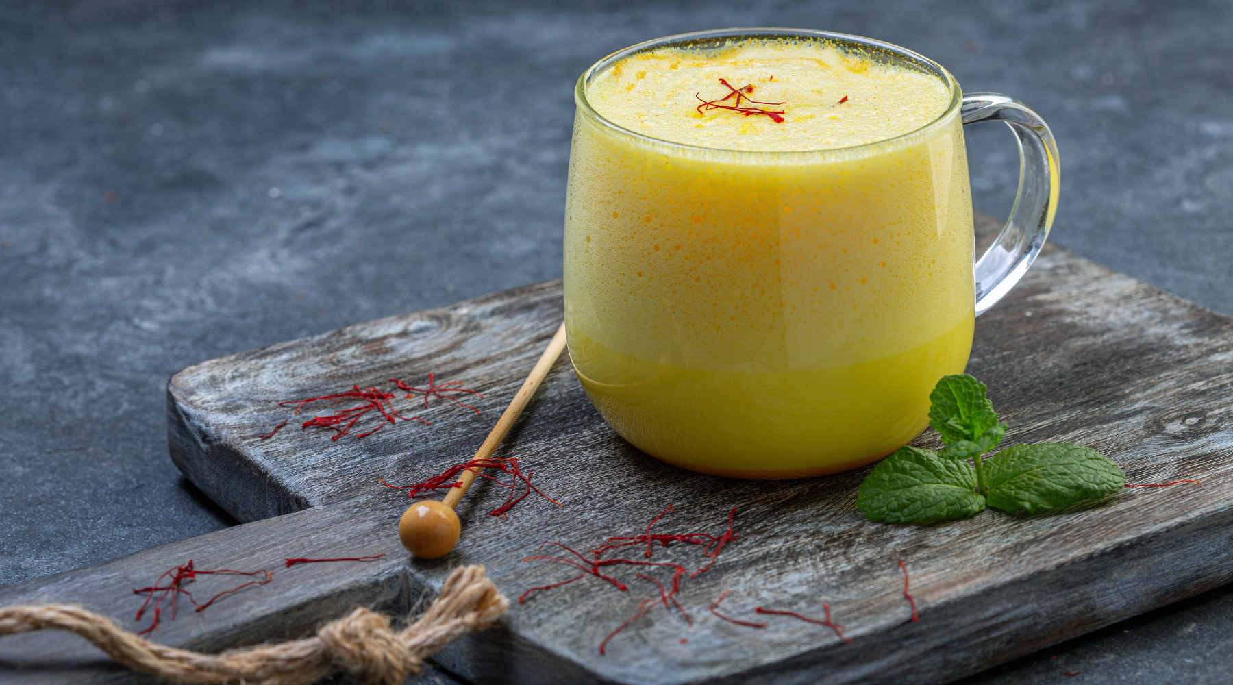 A glass of saffron milk, a yellow drink, placed on a wooden board.