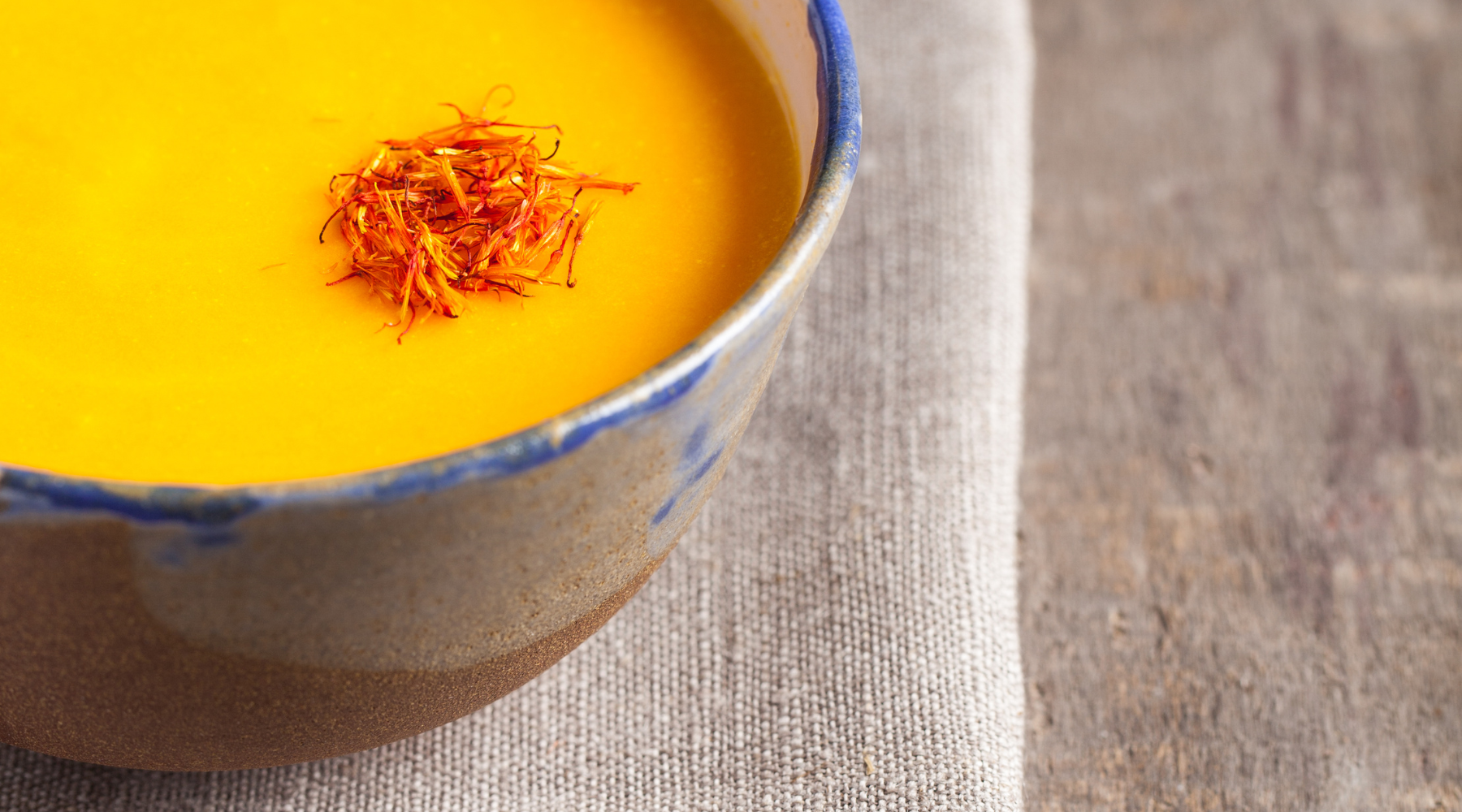 A bowl of pumpkin saffron soup garnished with a sprig of saffron, creating a vibrant and flavorful dish.