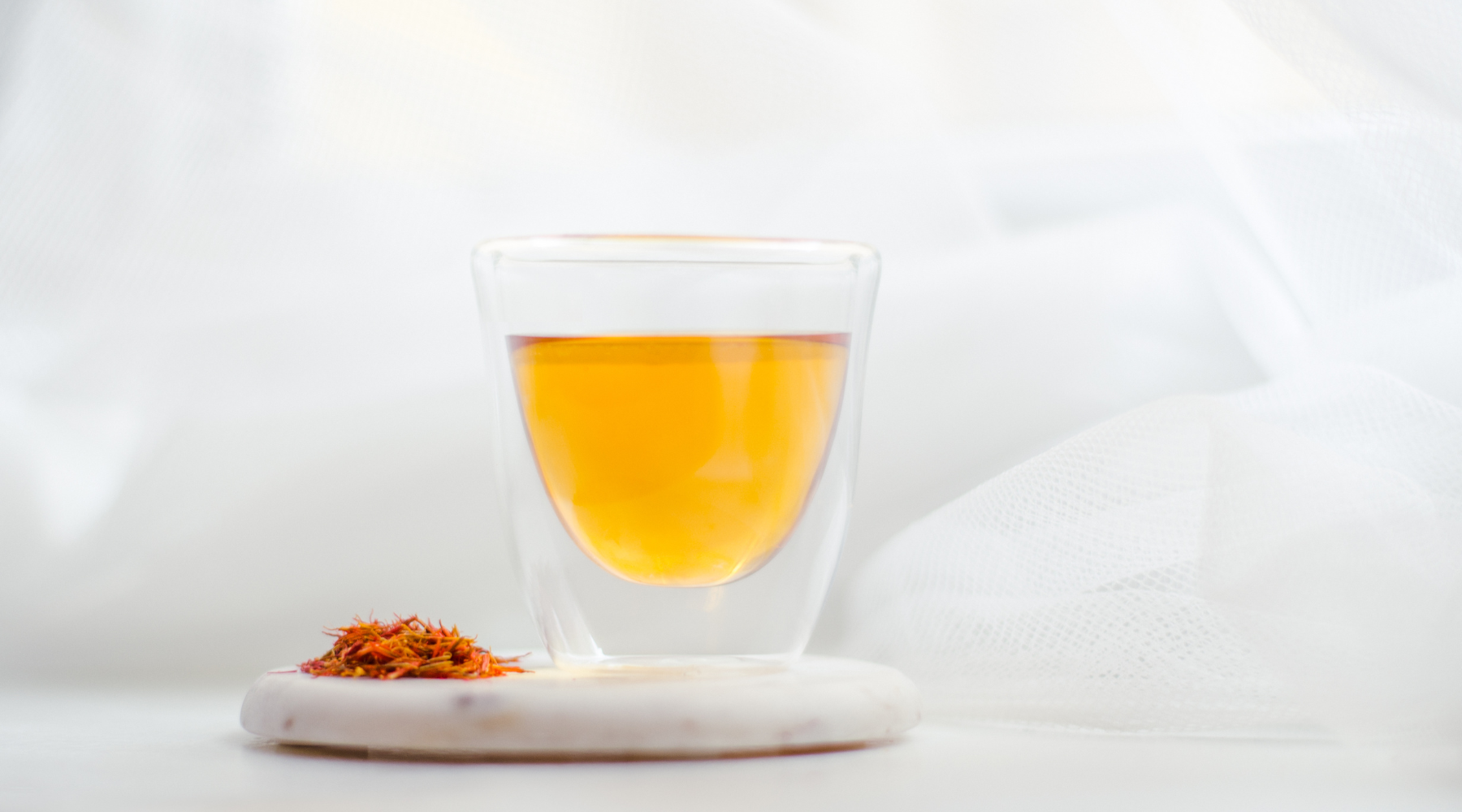 A glass of saffron infused tea on a white table next to saffron