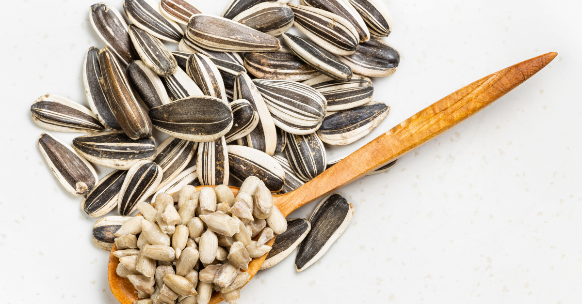 unshelled sunflower seeds on a white background with a wooden spoon of shelled sunflower seeds