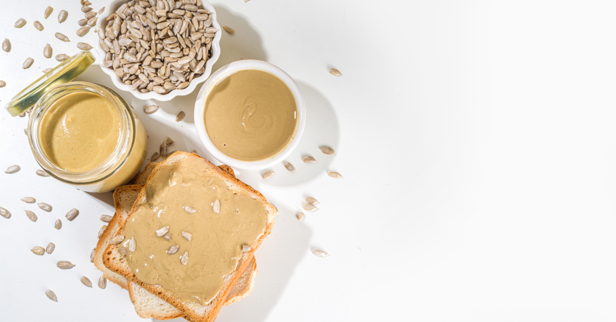 slice of bread spread with sunflower seed butter next to a jar of sunflower seed butter and a bowl of shelled sunflower seeds