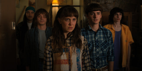 Photo of young teenage friends (one brown boy, one white girl, and three white boys) dressed in 70s fashion standing together to face a challenge. 
