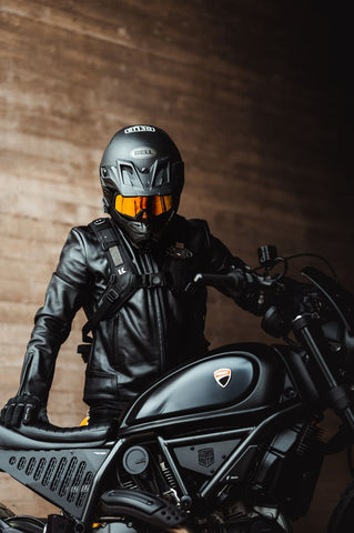 man standing beside his black motorbike, wearing a black leather motorcycle jacket and helmet