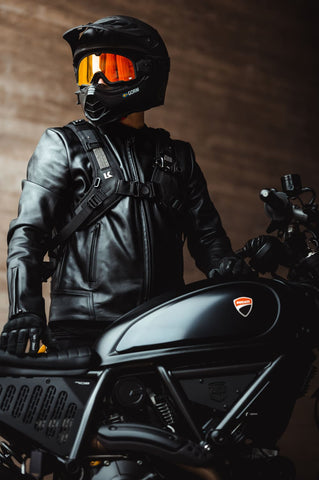 man wearing a motorcycle helmet with an orange visor while standing beside a black motorcycle